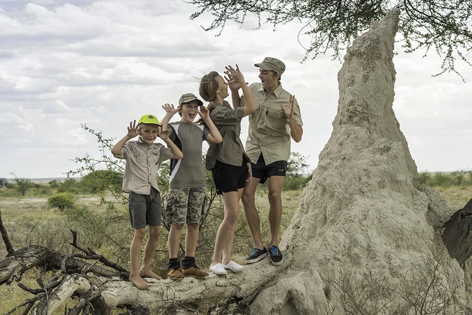 Family having fun beside a large termite mound at Onguma Nature Reserve, Namibia