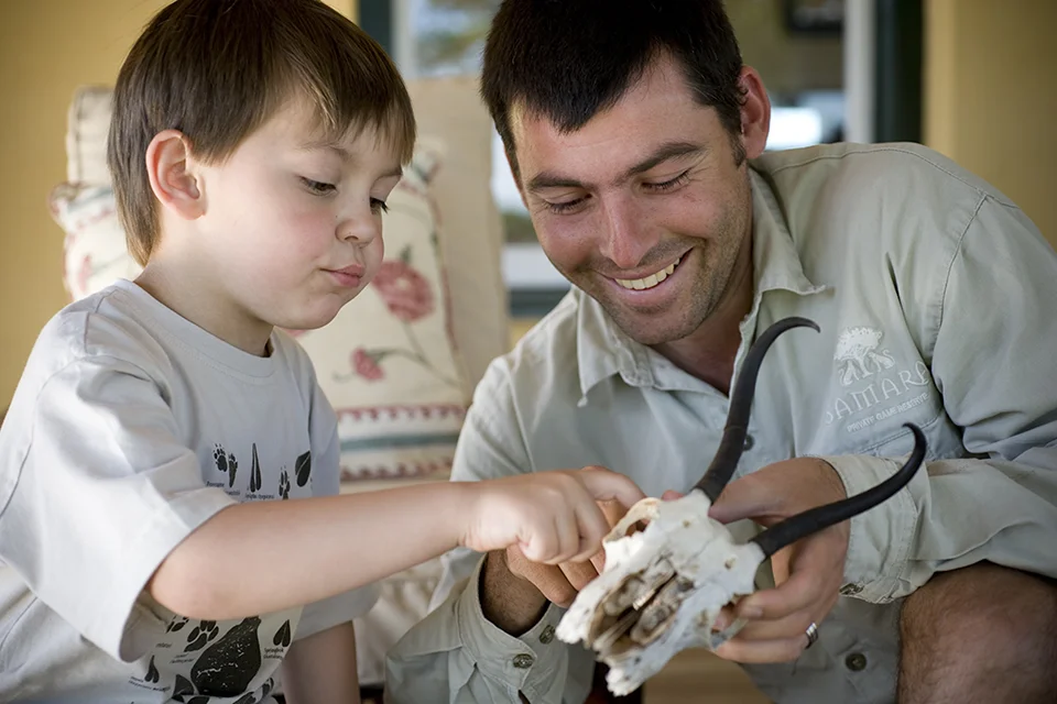 A young boy examines an animal skull with a smiling safari guide during an educational wildlife activity
