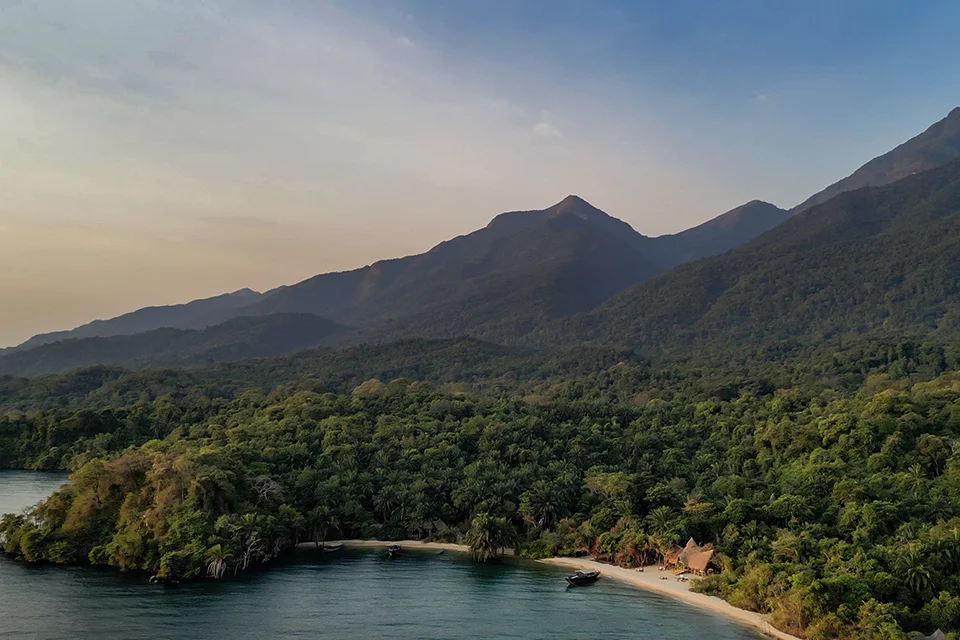 An aerial view of Mahale Mountains National Park, Tanzania, showing lush forest, sandy beaches and the shoreline of Lake Tanganyika backed by dramatic mountain peaks