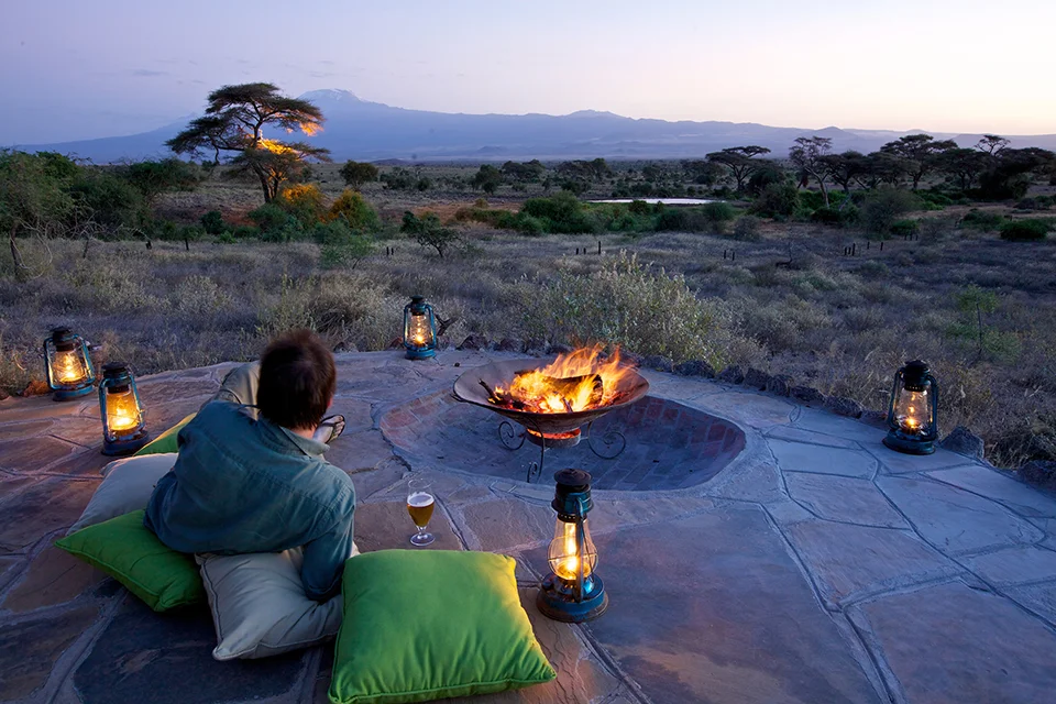 Guest enjoying sundowners by a campfire overlooking the Amboseli plains in Kenya