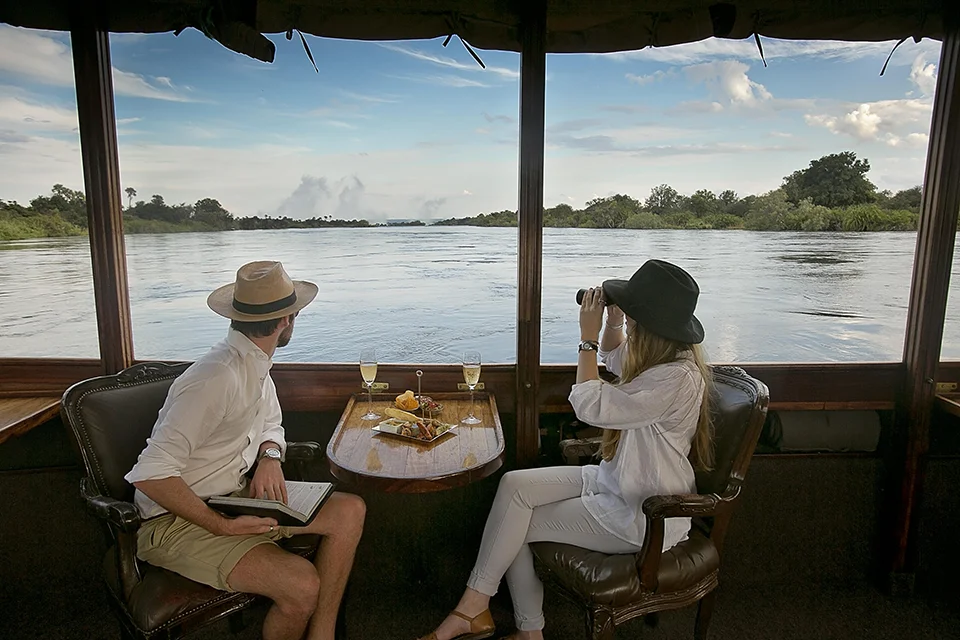 Couple enjoying drinks and wildlife viewing aboard a river cruise near Victoria Falls, Zimbabwe