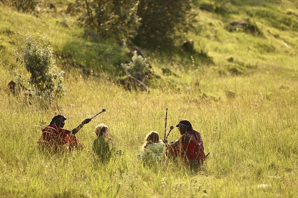 Maasai guides teaching children traditional skills in a grassy savannah