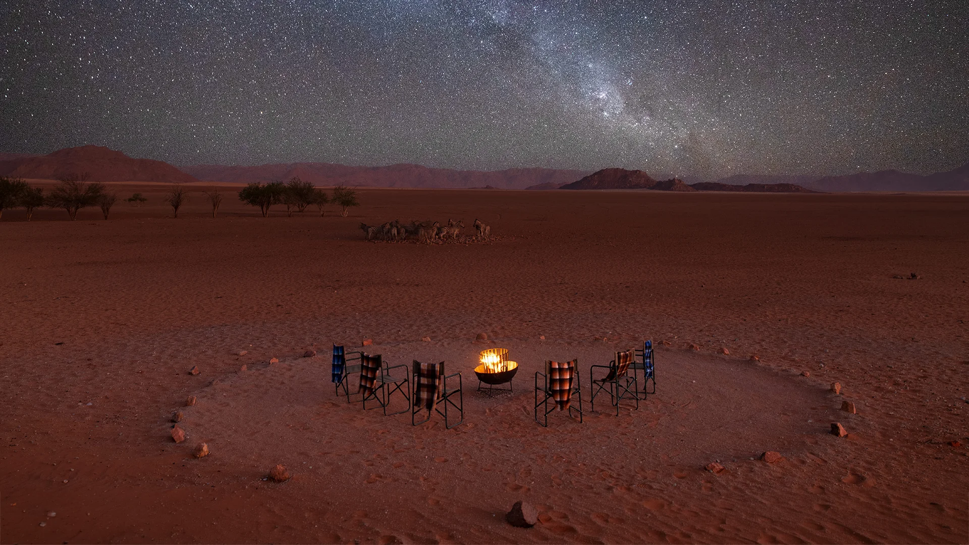 Campfire surrounded by safari chairs beneath the Milky Way at Kwessi Dunes in Namibia’s NamibRand Nature Reserve