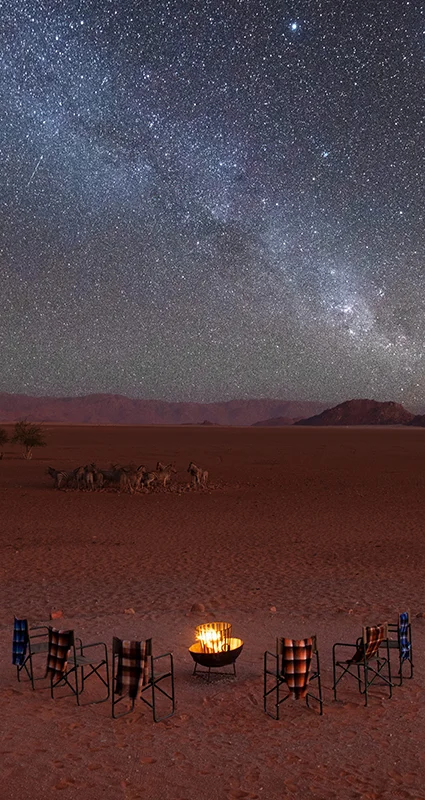 Campfire surrounded by safari chairs beneath the Milky Way at Kwessi Dunes in Namibia’s NamibRand Nature Reserve
