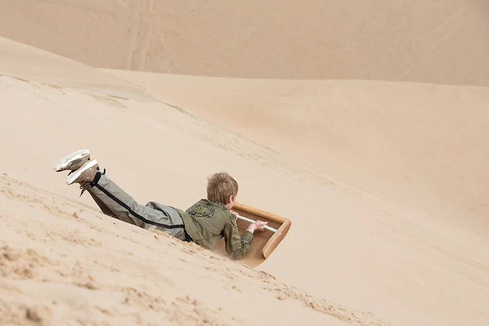 Child sandboarding down the dunes near Shipwreck Lodge on Namibia's Skeleton Coast