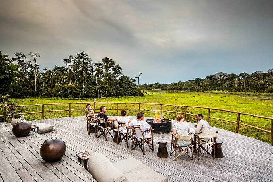 Guests relaxing around a fire pit on the deck overlooking Lango Bai at Lango Camp in Odzala-Kokoua National Park, Republic of the Congo
