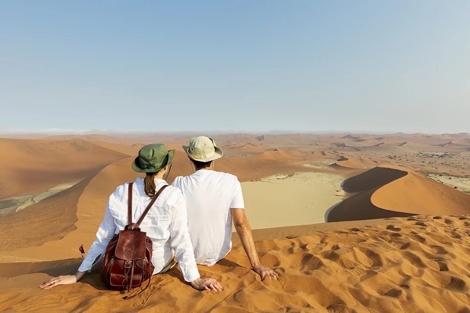 Couple sitting on a high dune overlooking the red sands of Sossusvlei in Namibia