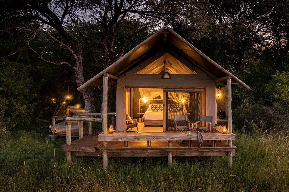 Luxury safari tent with a private deck surrounded by woodland at Little Sable, Botswana