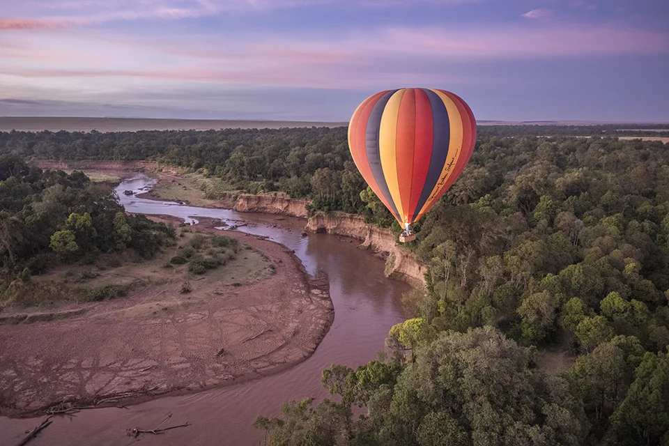 Hot air balloon drifting over the Mara River at sunrise in the Maasai Mara