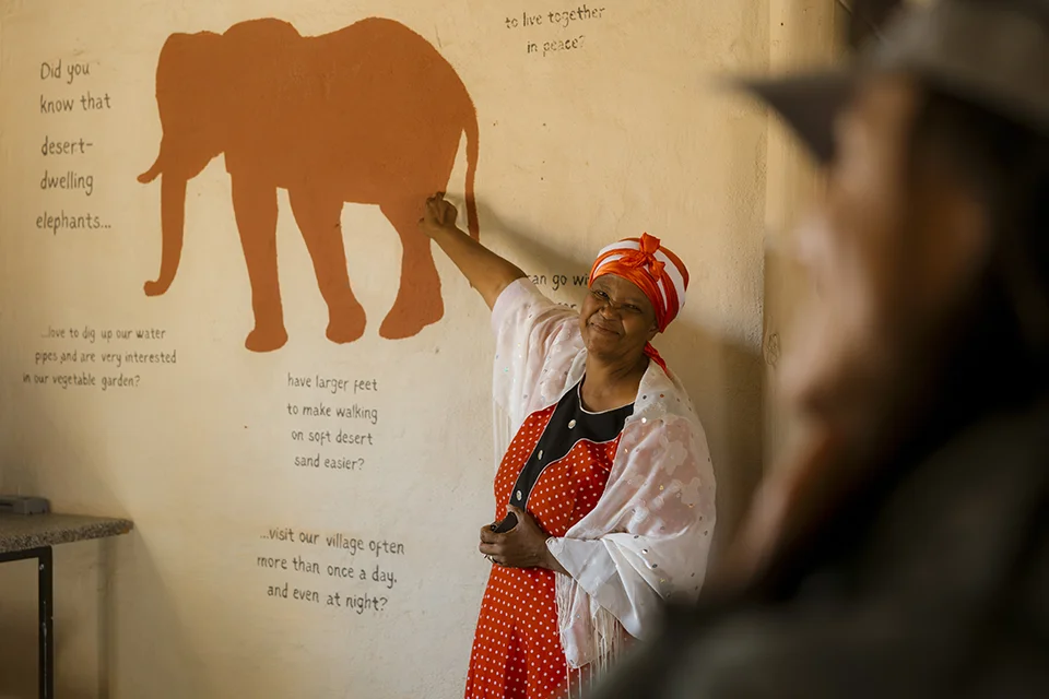 Local woman explaining desert-adapted elephants to safari guests during a community visit to De Riet village near Wilderness Damaraland Camp in Namibia