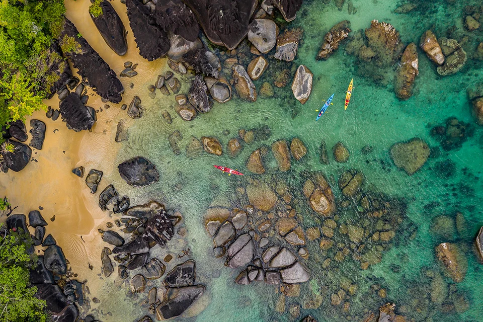 Sea kayakers paddling through shallow turquoise waters along a rocky island shoreline