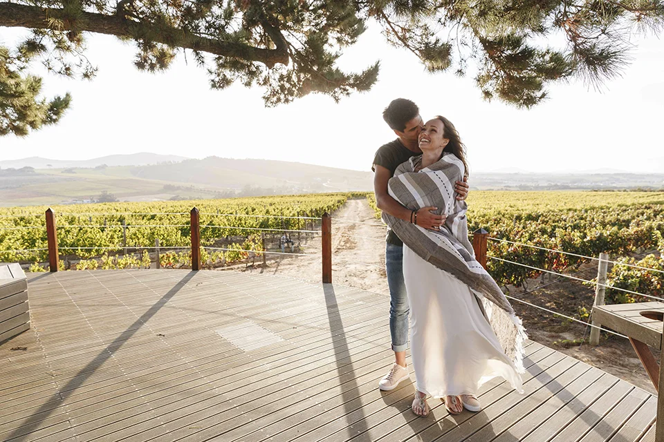 Couple embrace on a vineyard deck overlooking rolling Cape Winelands vineyards, enjoying a romantic escape that pairs perfectly with a South African honeymoon safari