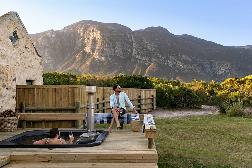 Couple relax in a private wood-fired hot tub with mountain views in the Western Cape, a romantic addition to a South African honeymoon safari itinerary