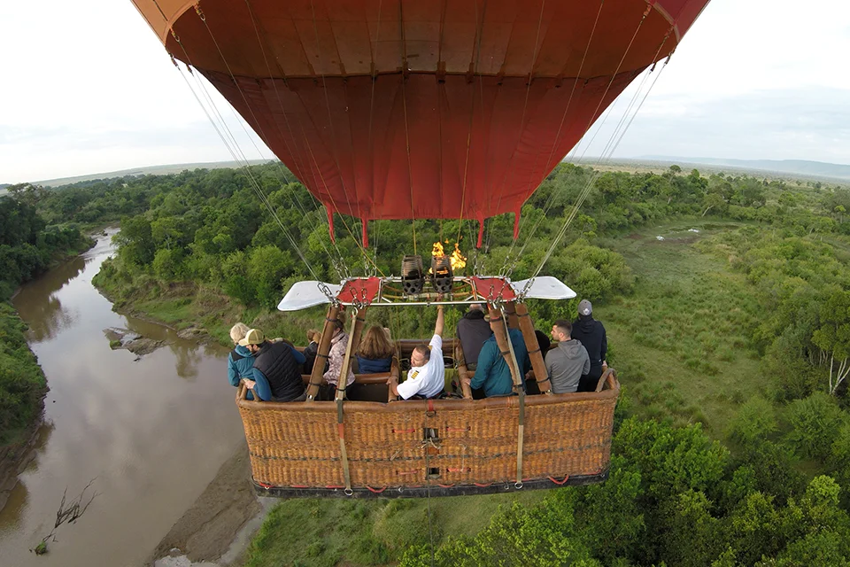 Hot air balloon carrying safari guests over the Mara River and surrounding plains in the Maasai Mara, Kenya