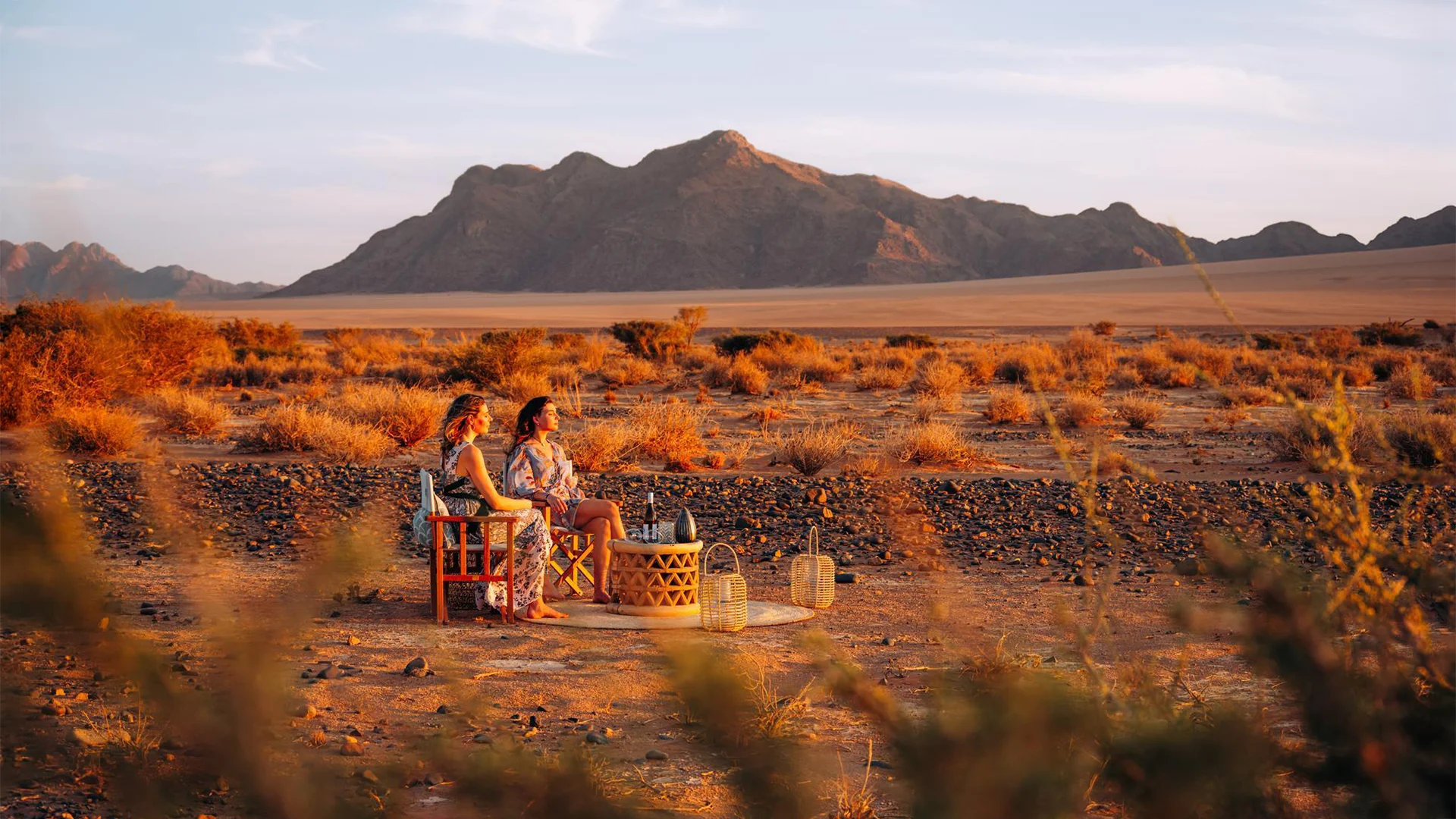 Guests enjoying sundowners in the desert near Kulala Desert Lodge, Namibia, with rugged mountains in the background