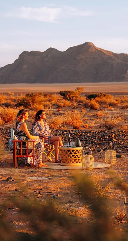 Guests enjoying sundowners in the desert near Kulala Desert Lodge, Namibia, with rugged mountains in the background