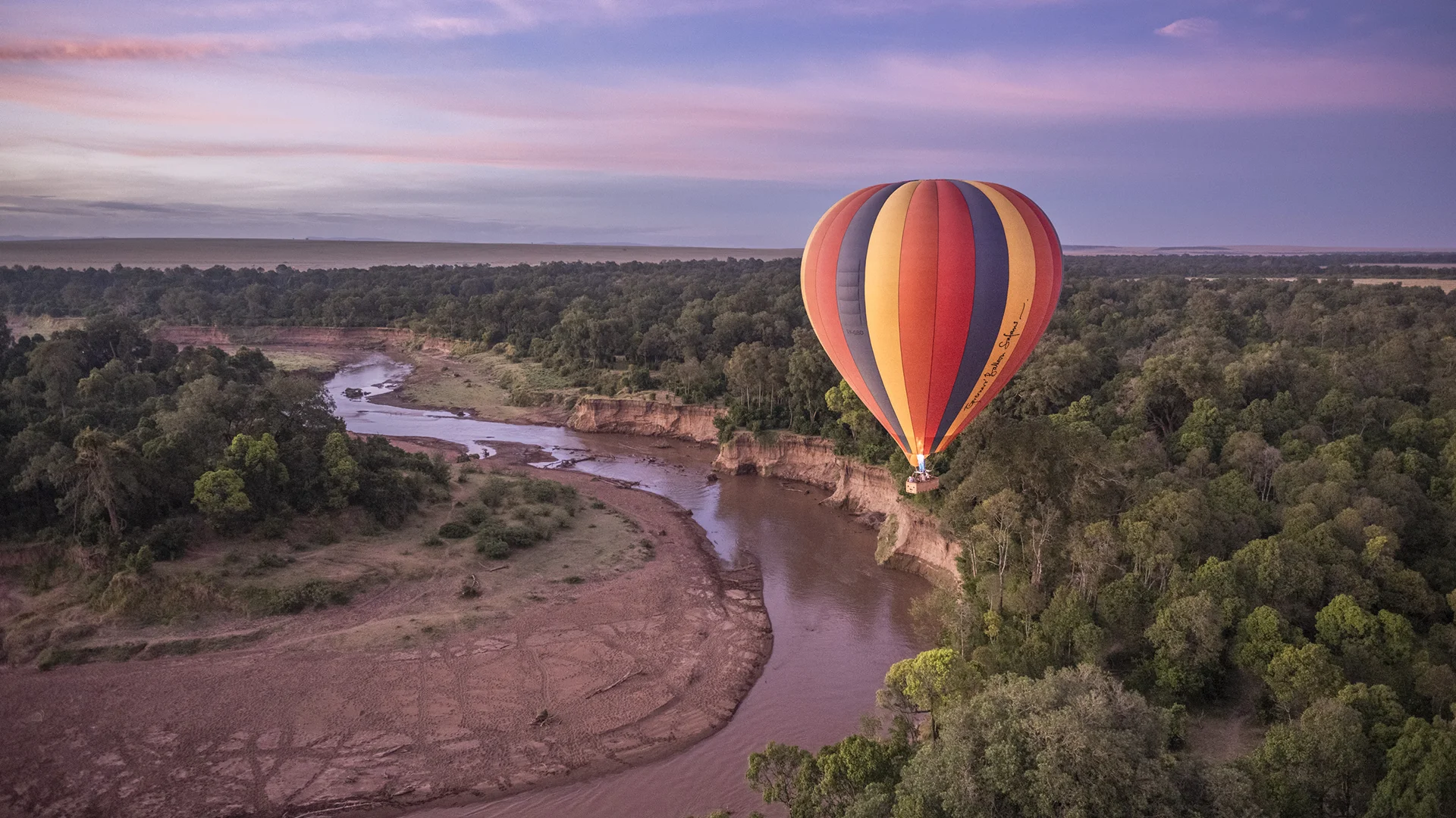 Hot air balloon floating over the Mara River at sunrise in Kenya's Maasai Mara National Reserve