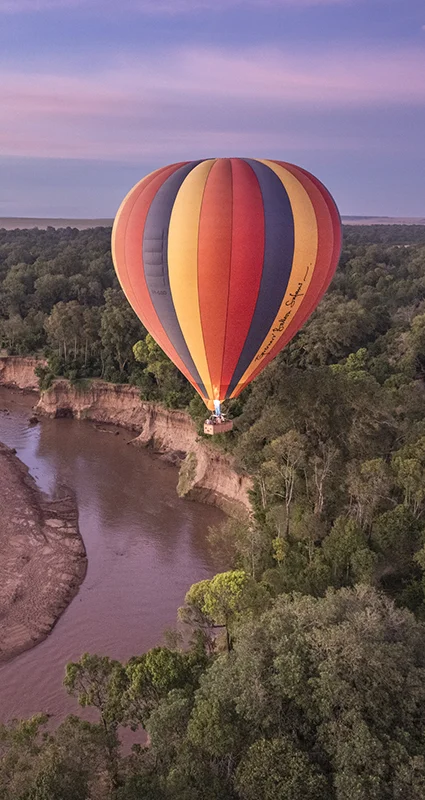 Hot air balloon floating over the Mara River at sunrise in Kenya's Maasai Mara National Reserve