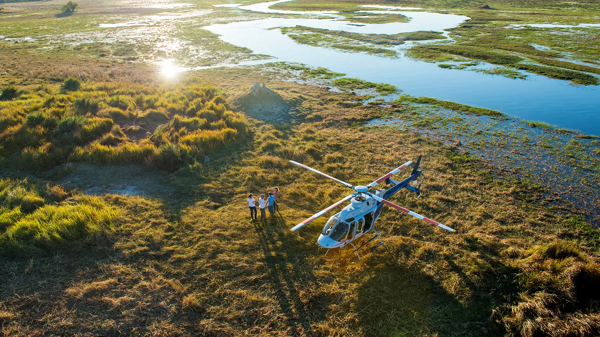 Helicopter landed beside the Okavango Delta wetlands in Botswana, with guests enjoying a scenic stop overlooking winding channels