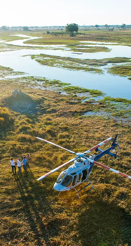 Helicopter landed beside the Okavango Delta wetlands in Botswana, with guests enjoying a scenic stop overlooking winding channels