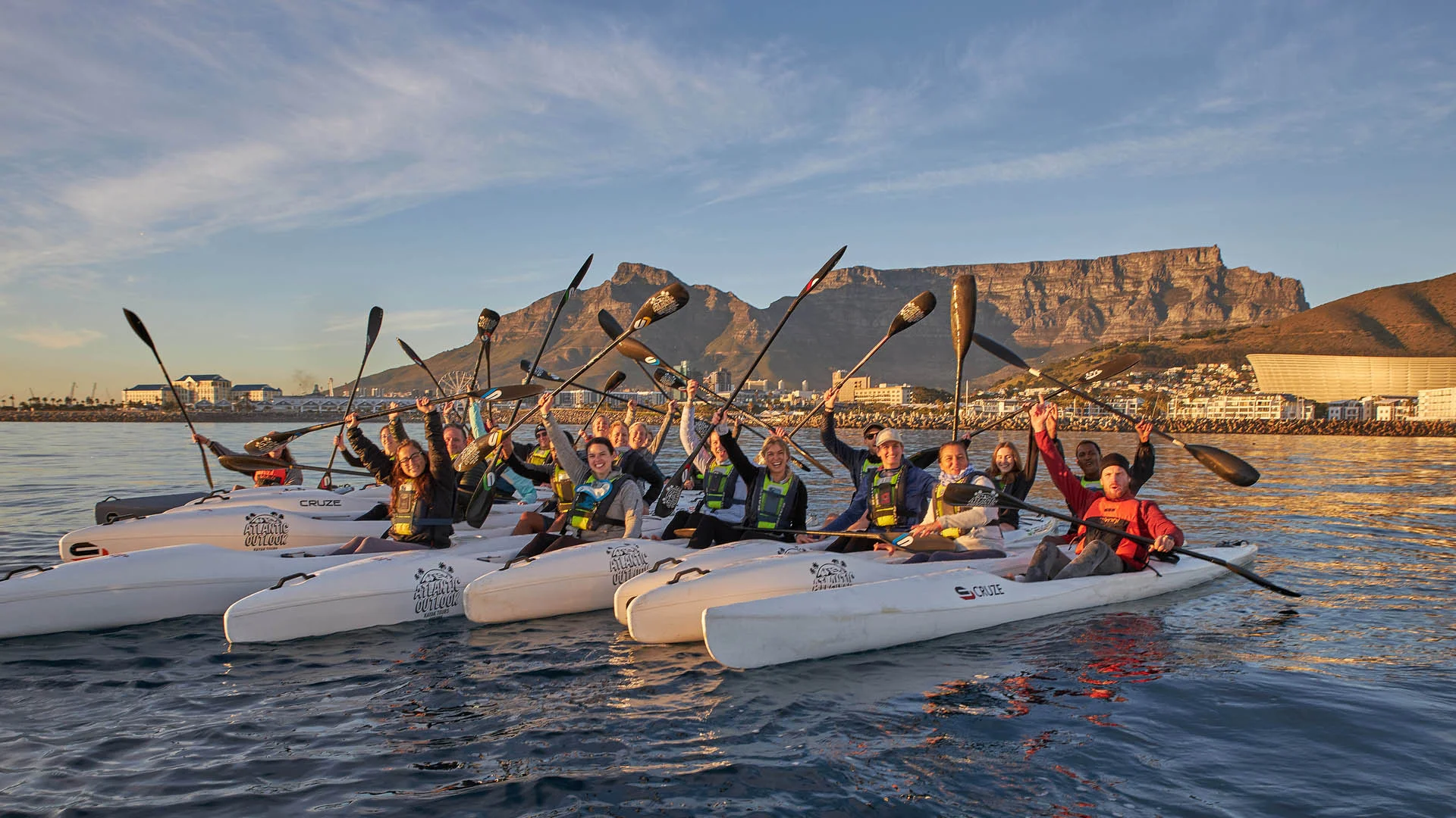 Group of kayakers raising their paddles with Table Mountain in the background, Cape Town