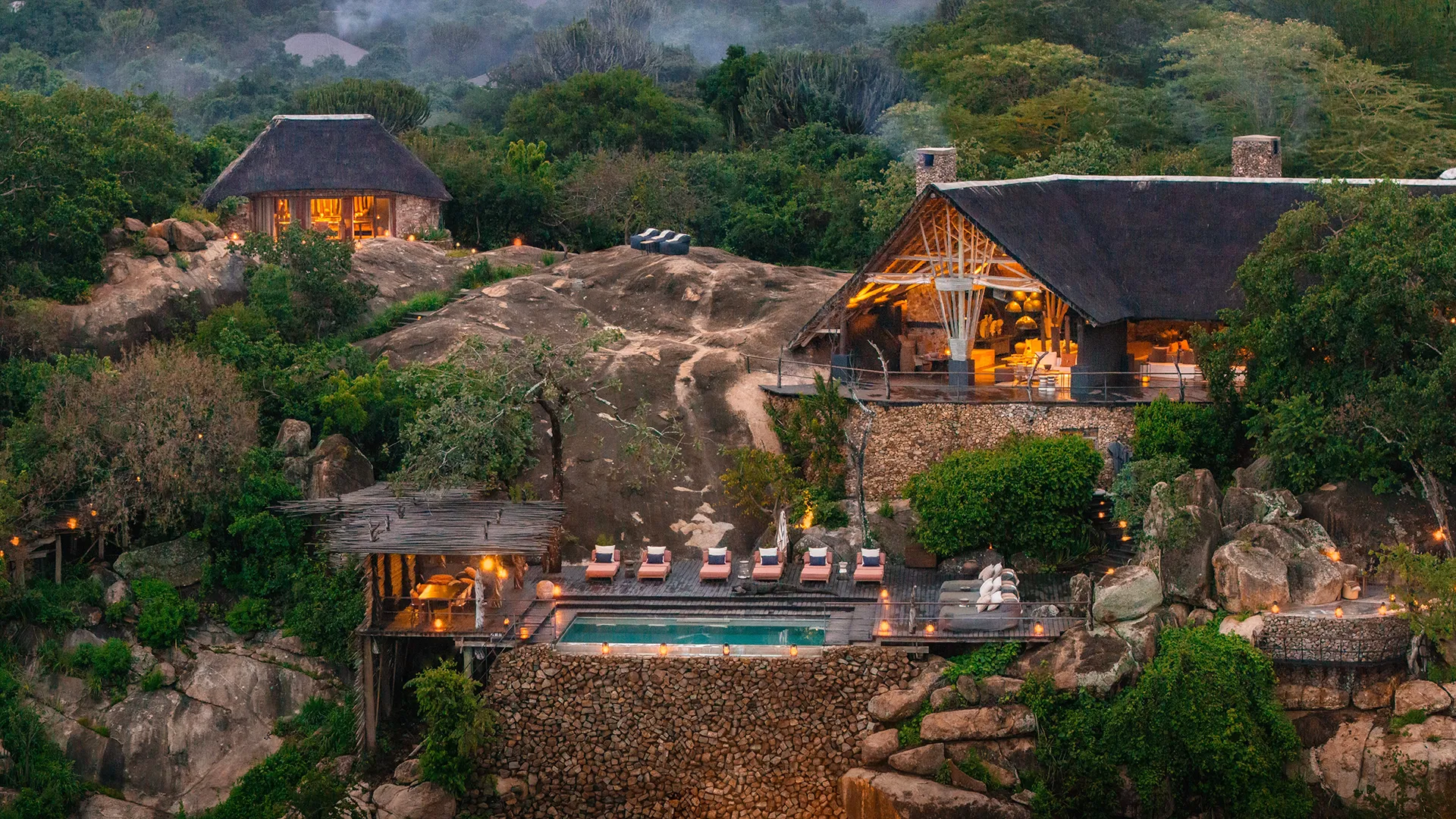 Mwiba Lodge nestled among rocky outcrops and lush vegetation, with a swimming pool and thatched-roof buildings