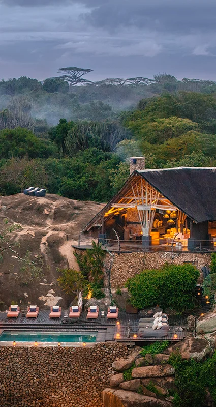 Mwiba Lodge nestled among rocky outcrops and lush vegetation, with a swimming pool and thatched-roof buildings