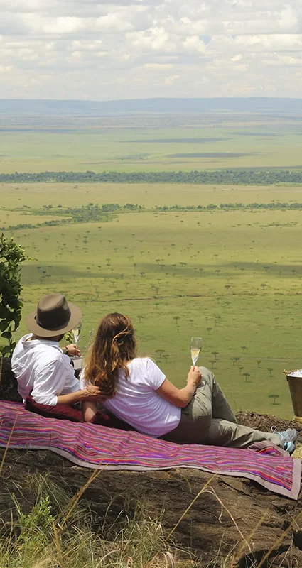 Couple enjoy a private champagne picnic overlooking the vast Masai Mara plains, a romantic highlight of a luxury Kenya honeymoon safari