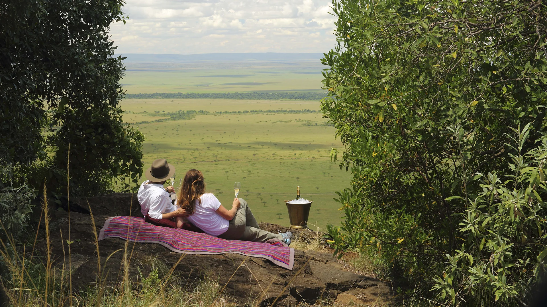 Couple enjoy a private champagne picnic overlooking the vast Masai Mara plains, a romantic highlight of a luxury Kenya honeymoon safari