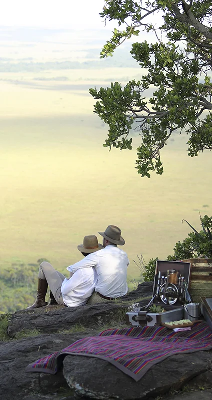 Couple enjoying a private picnic overlooking the Maasai Mara from the Out of Africa kopje at Angama Mara, Kenya