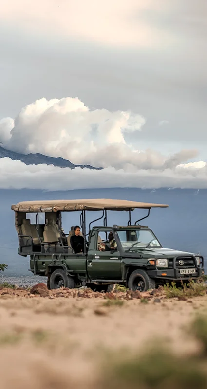 Safari vehicle on the Amboseli plains with Mount Kilimanjaro rising above the clouds in the background