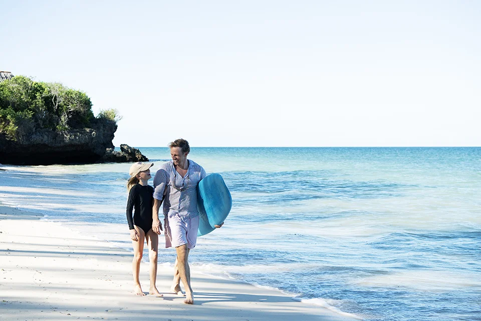 An adult and child walk along the shoreline at Diani Beach, Kenya, enjoying a relaxed day beside the Indian Ocean