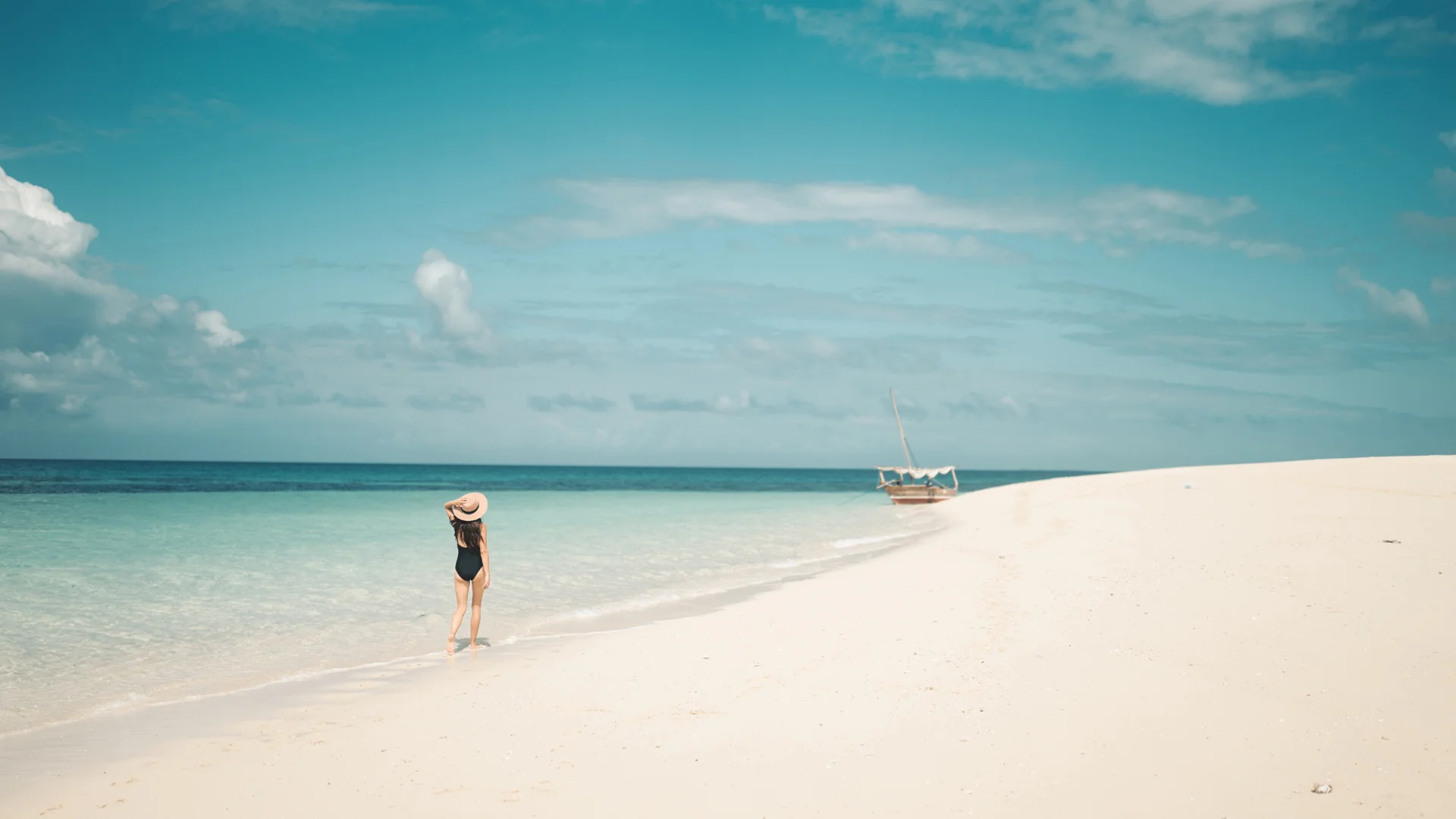 Woman walking along a white-sand beach beside turquoise waters in Zanzibar, Tanzania